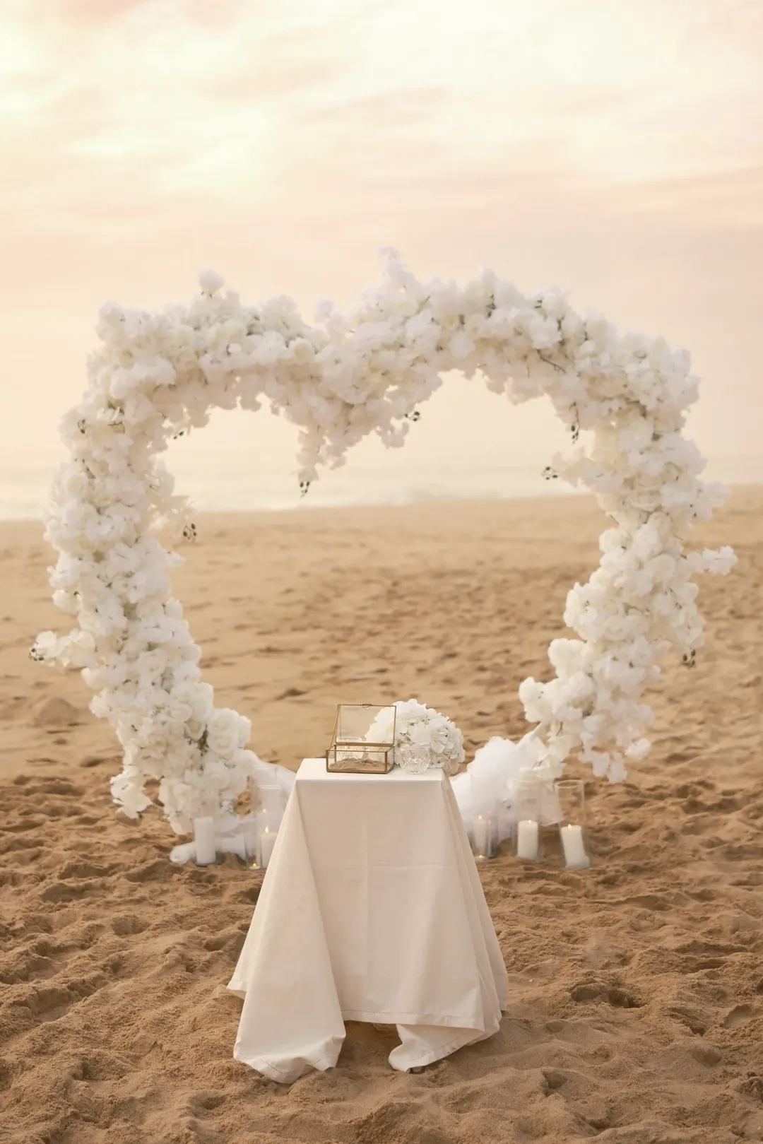 The heart-shaped arch of white flowers on the sand, before the ceremony