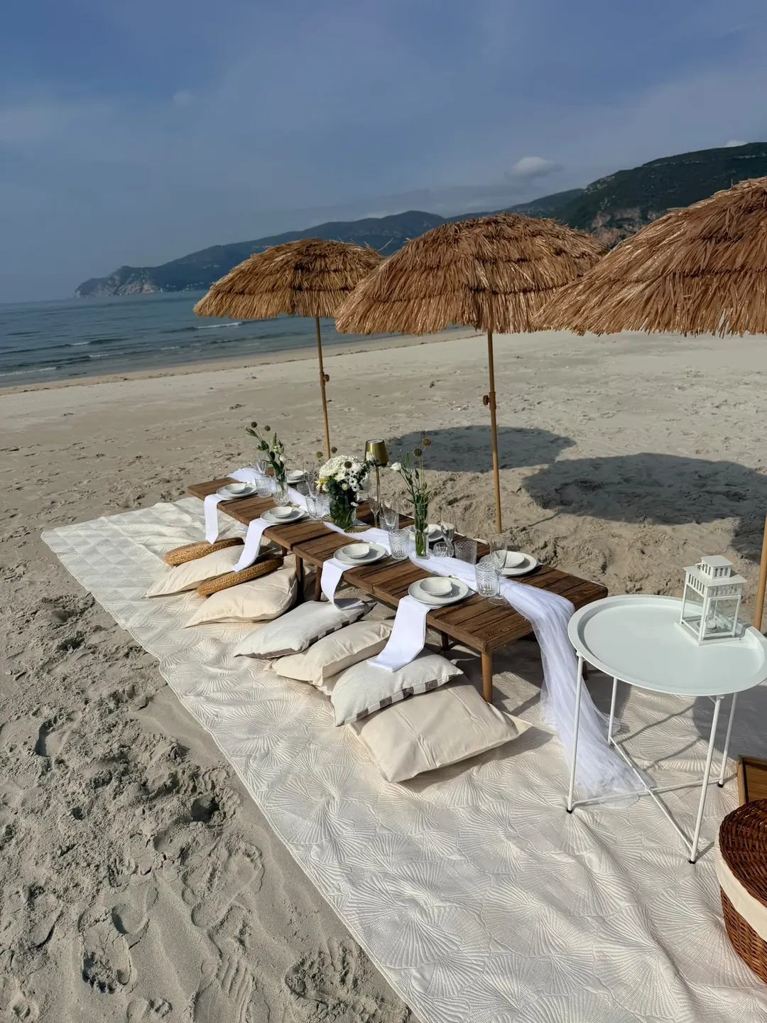 A long low table set for a private celebration on the beach, under straw parasols