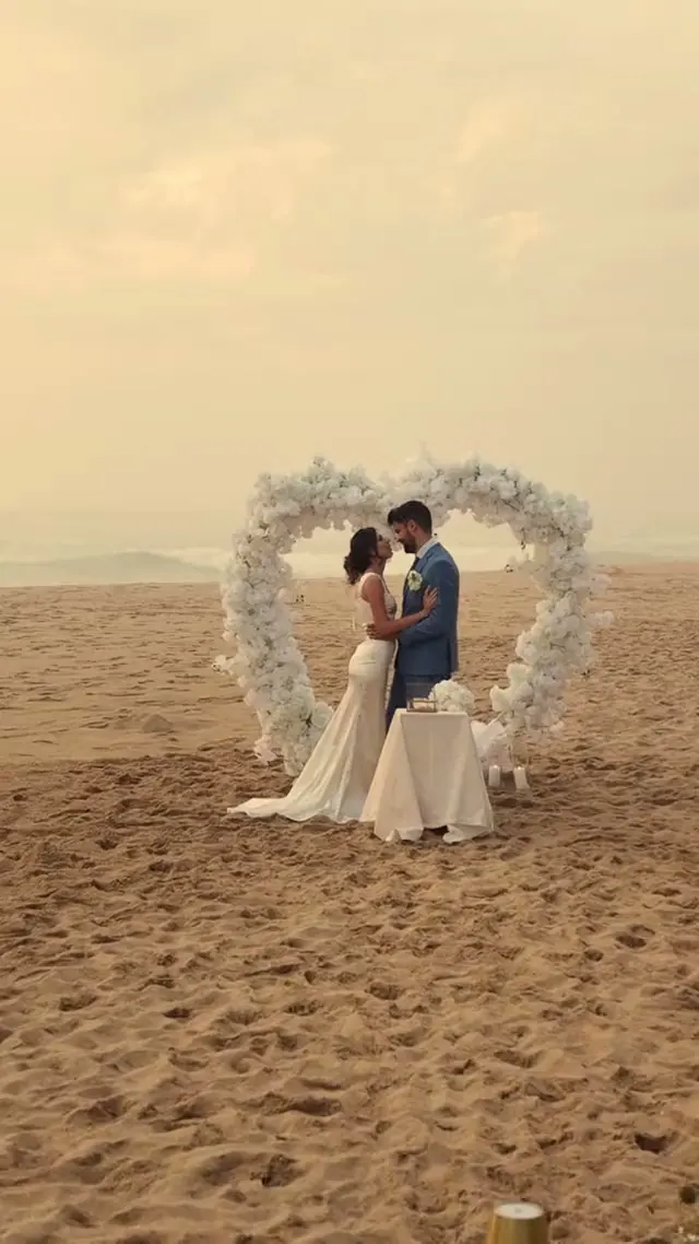 The couple at a heart-shaped arch of white flowers on the beach