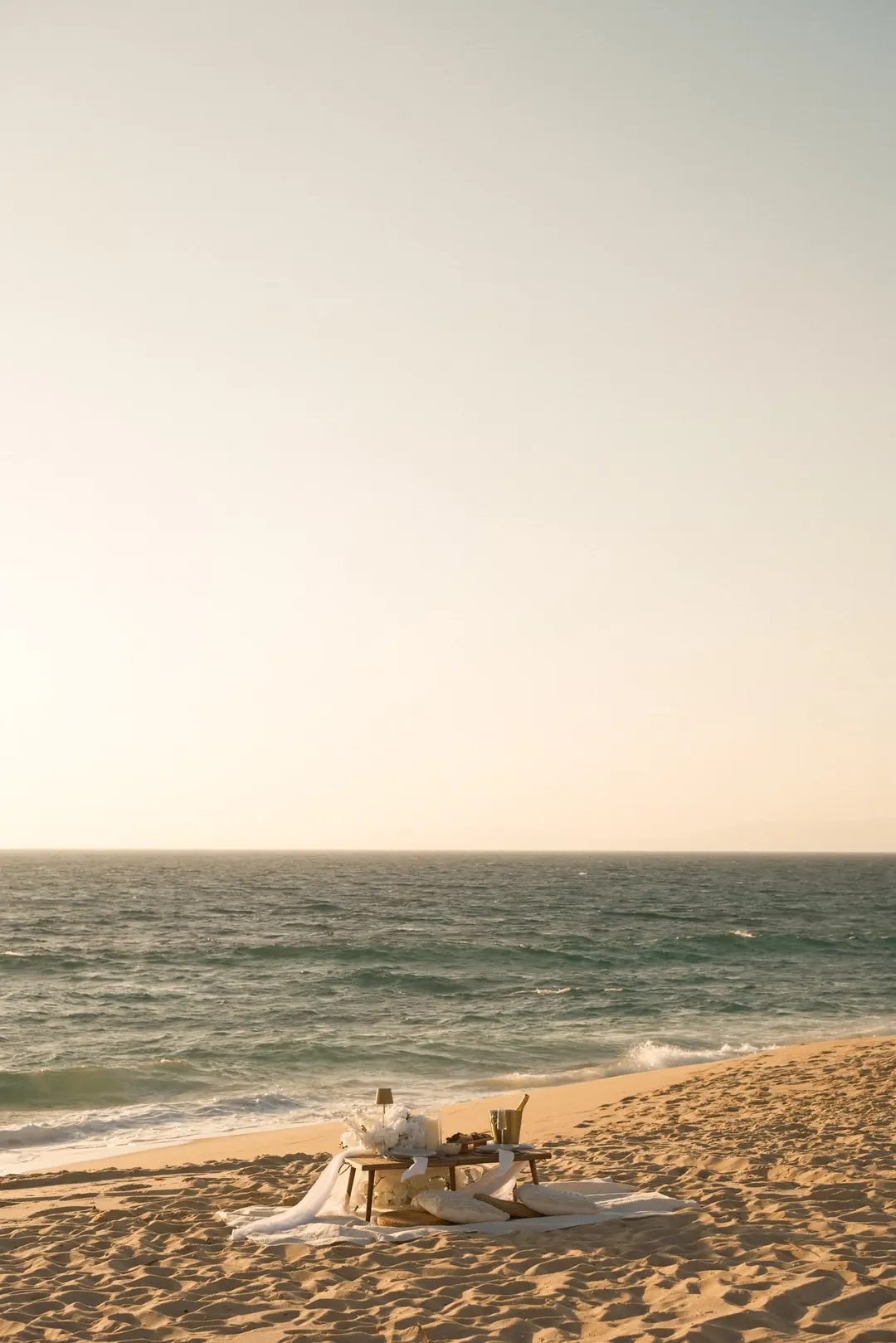 A low table with cushions set on the beach at golden hour, the sea behind it