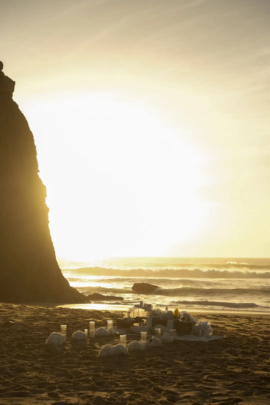 Candles on the sand below a cliff as the sun sets over the sea