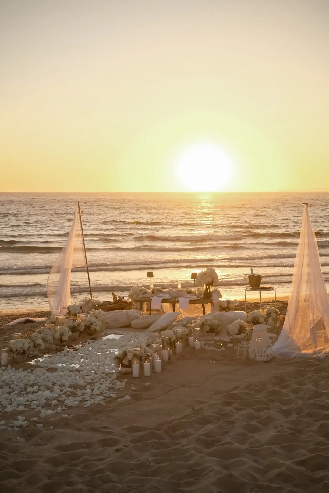 A proposal set-up on the sand at sunset, framed by linen sails and white petals